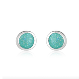 A pair of round stud earrings with glittery light blue-green centers and polished silver-toned bezels, shown on a clean white background with a soft reflection below.
