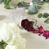 Burlap bag with dried red flowers on a light wooden surface with green leaves and white roses.